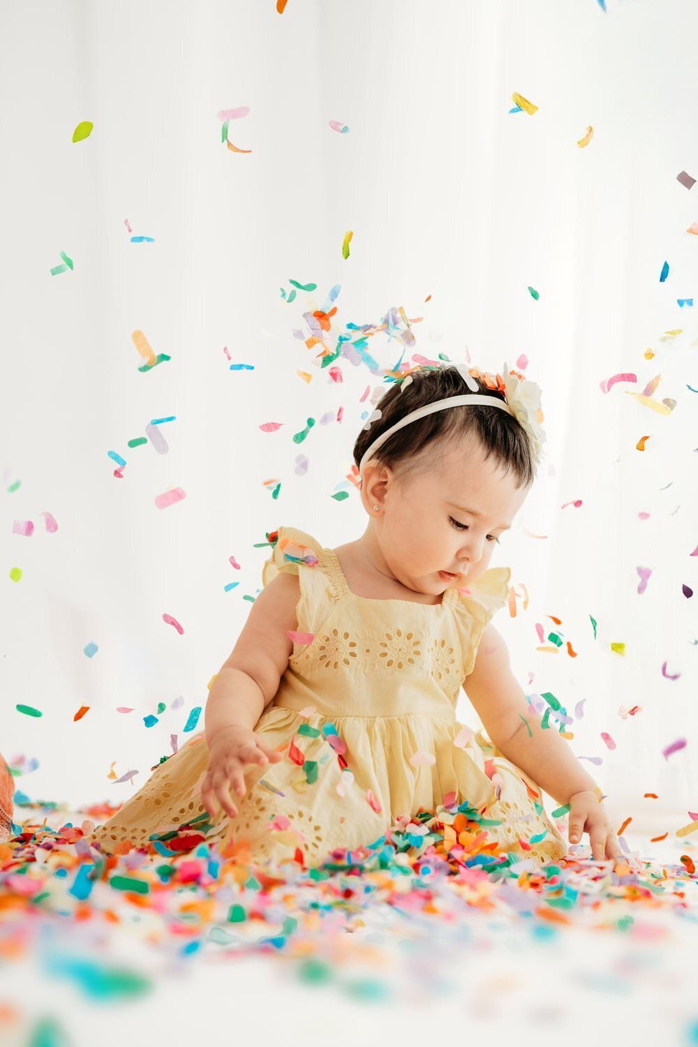 baby looks down at confetti as it falls all around her