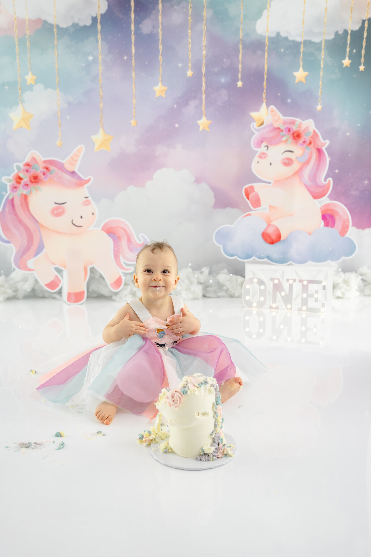 Girl in unicorn dress eating unicorn cake during themed cake smash session— captured by Alliston and Barrie cake smash photographer.