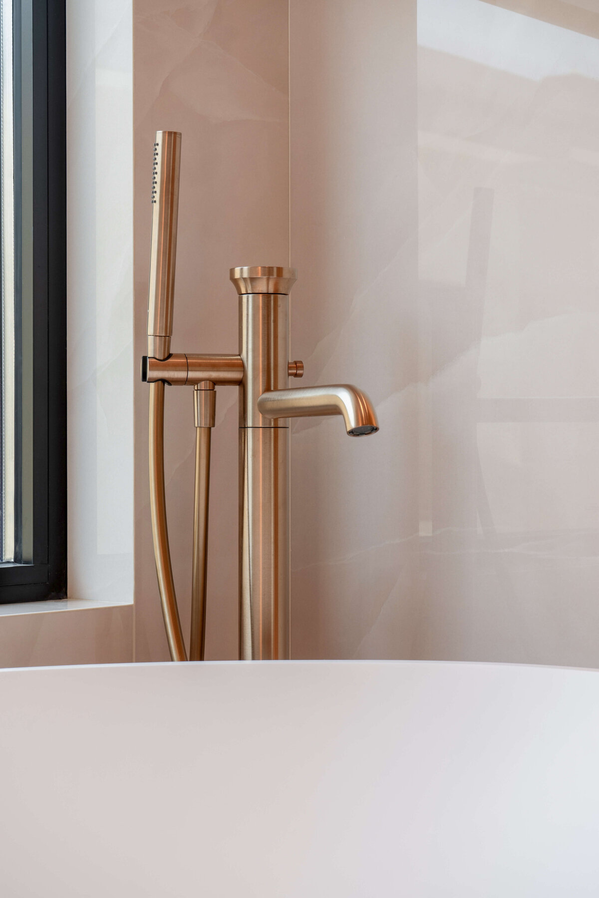 Large white soaking tub with a rose gold spout in a light pink marble bathroom.