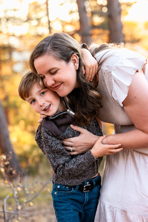A mom hugs her small son with yellow fall leaves in the background.