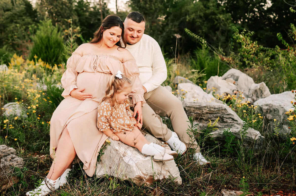 maternity picture in Springfield MO of pregnant couple sitting on rock with toddler