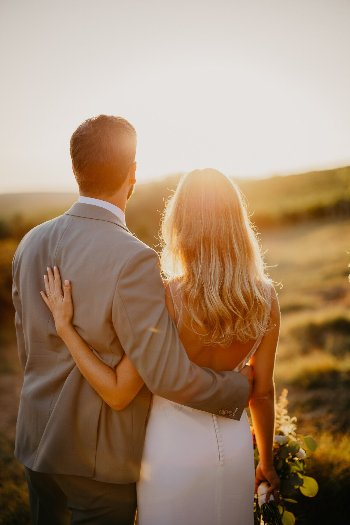 Bride and groom embracing at sunset with a view of the hills at Borgo Divino, intimate wedding in Tuscany.