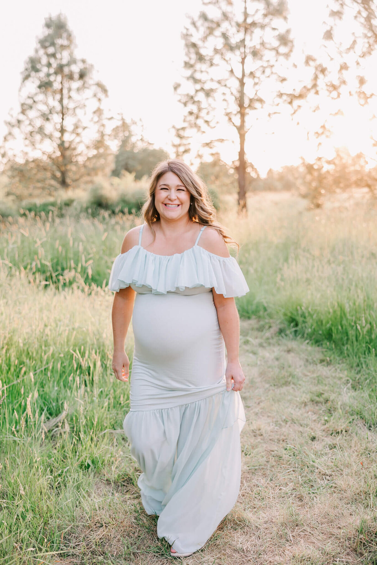 mom wearing green dress smiling walking towards camera in field in beaverton oregon