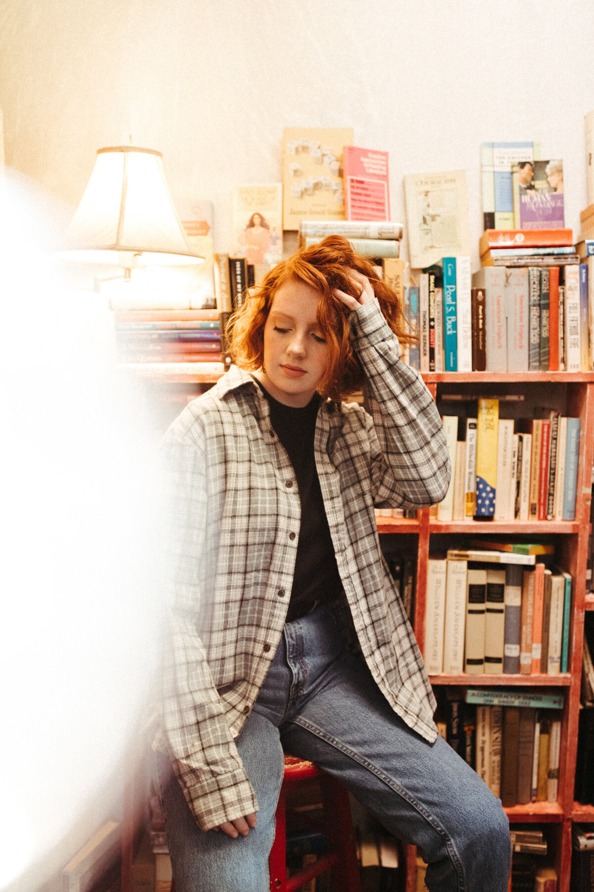 Girl senior wearing a flannel and sitting on a stool in a bookstore
