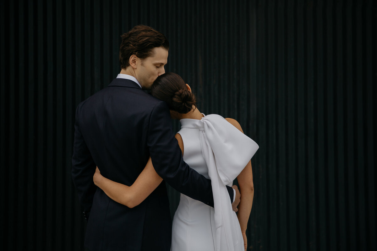 Bride and Groom with backs to camera facing black door with groom kissing bride's head