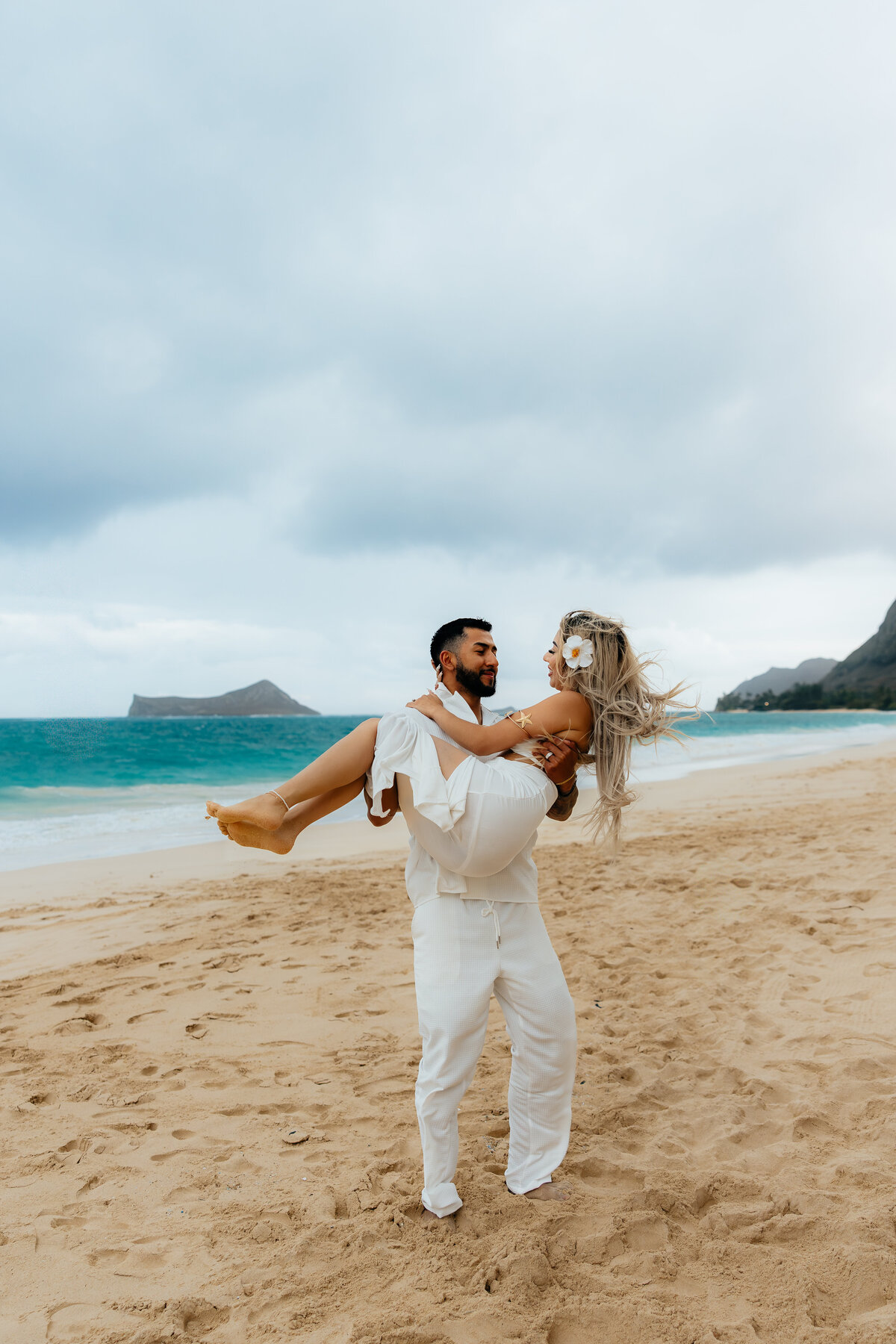 Husband lifting his wife during their honeymoon photoshoot on Waimanalo Beach in Oahu