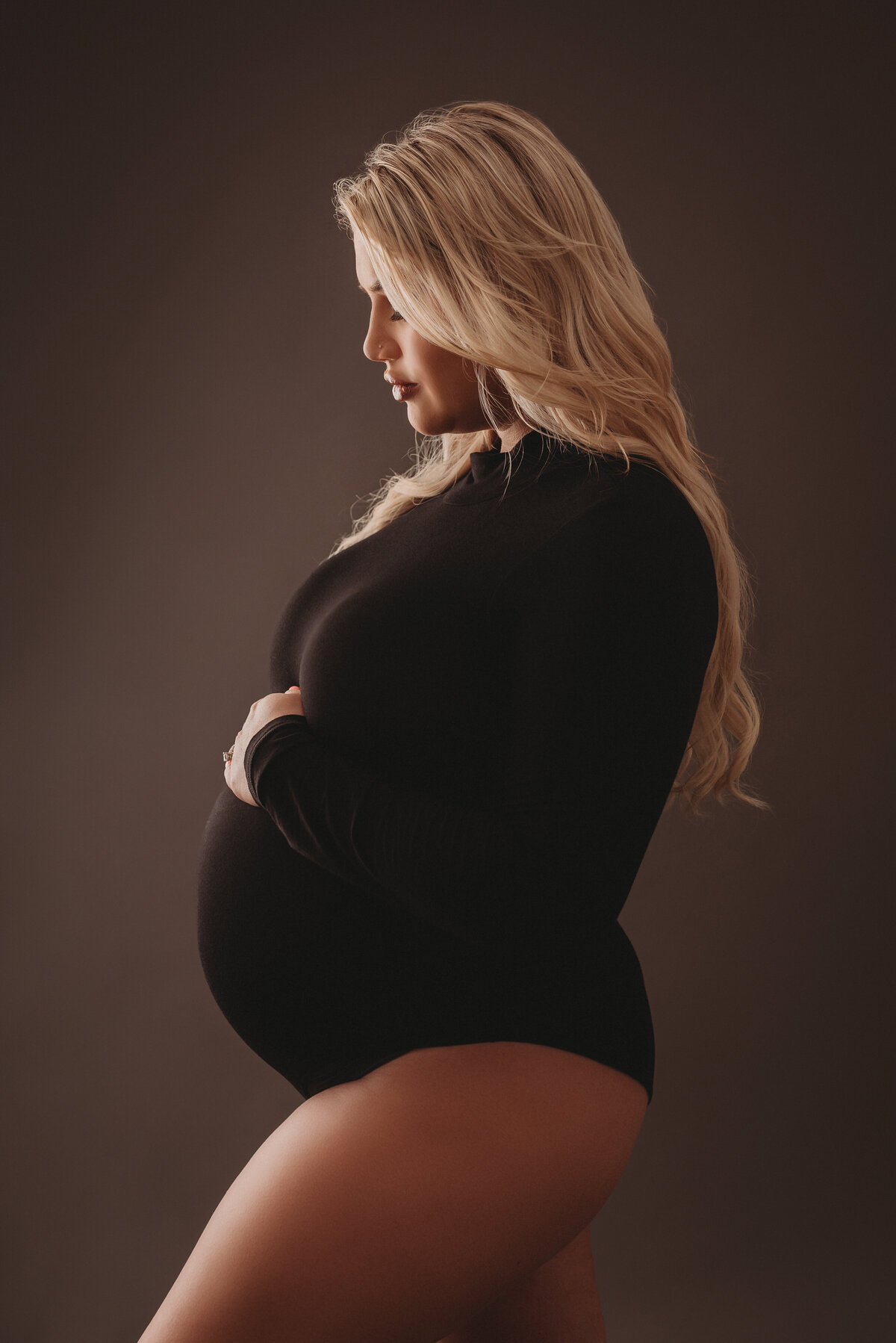 Atlanta, Georgia newborn photographer portrait session with pregnant woman at maternity session wearing black body suit on gray backdrop holding baby bump