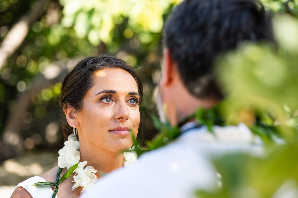 bride gazing atgroom during intimate ceremony with green foliage on the beach