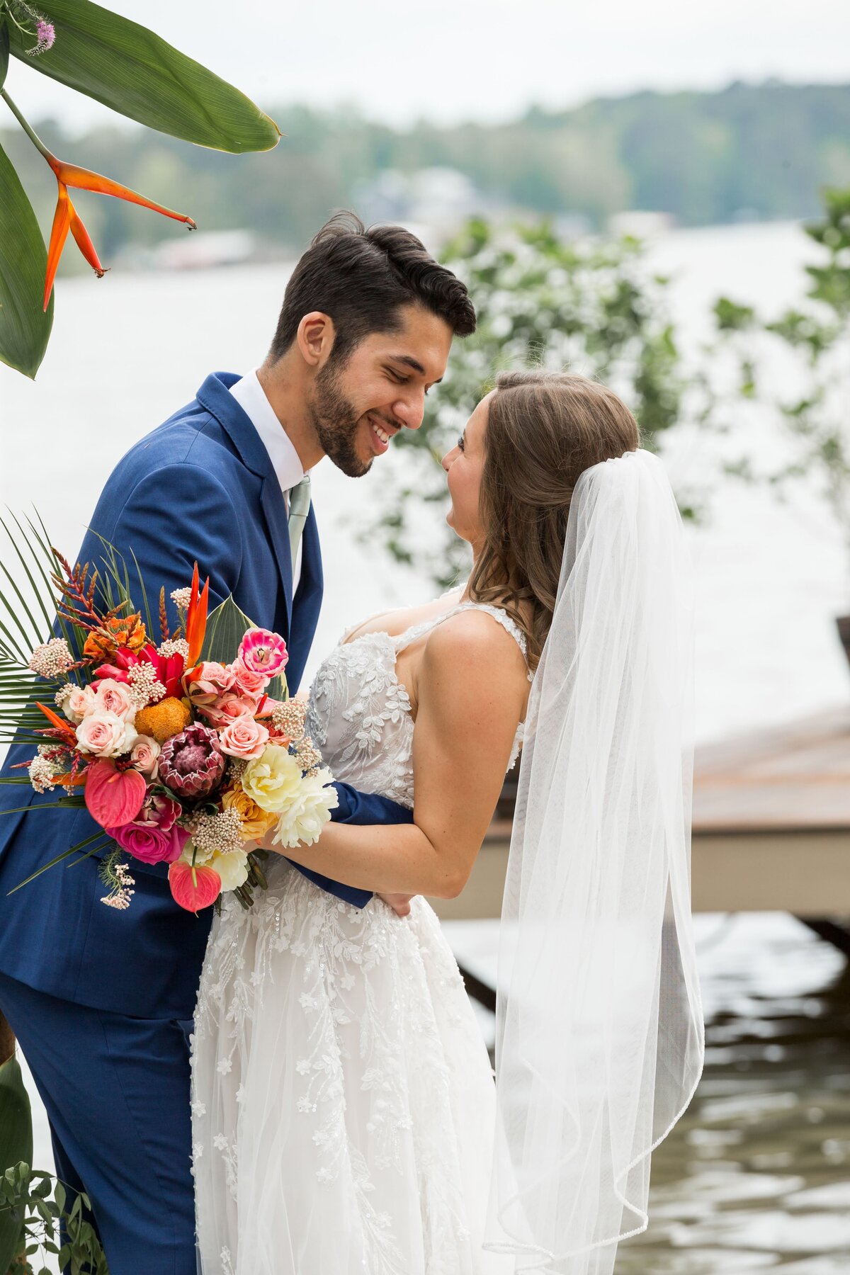 Man in blur suit leaning in to woman in white dress with veil and bouquet of flowers
