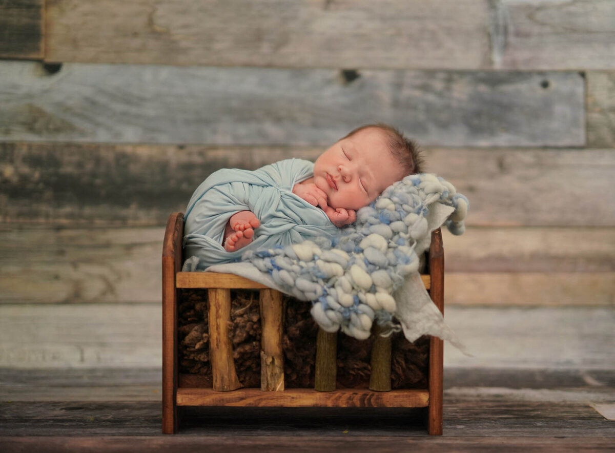 Newborn sleeping in a blue wool blanket and mini crib