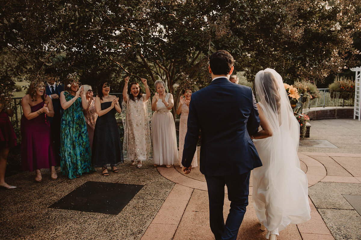 A newlywed couple walking towards a group of celebrating guests 
