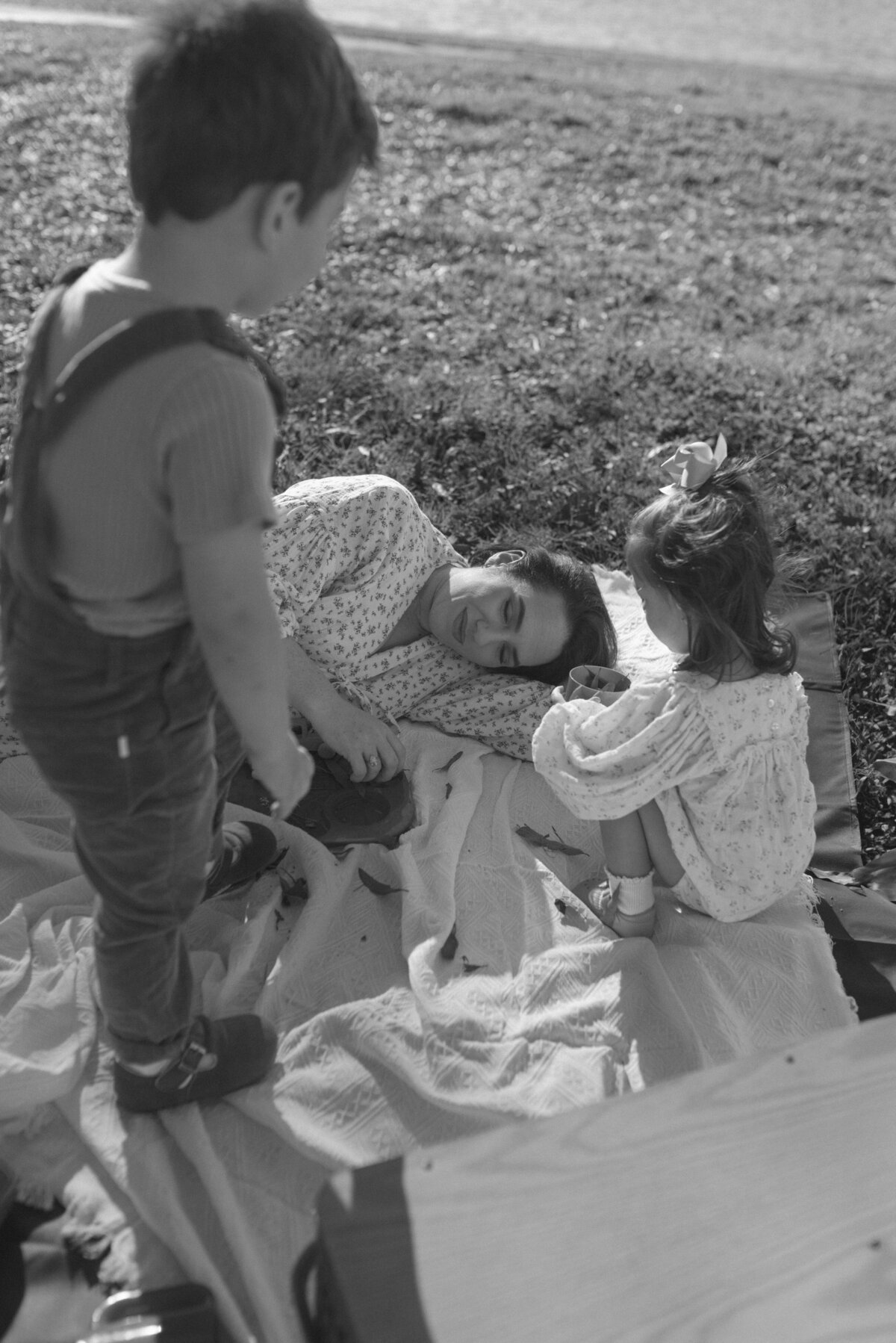 black and white photo of a mother and her two kids laying on a picnic blanket outside and playing with leaves.