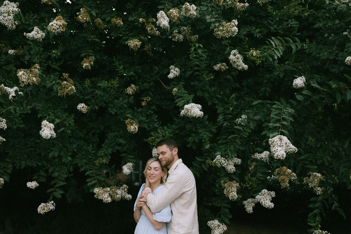 Couple holding each other in front of a flowering tree in North Carolina during the spring, by Andrea-Marie Photography