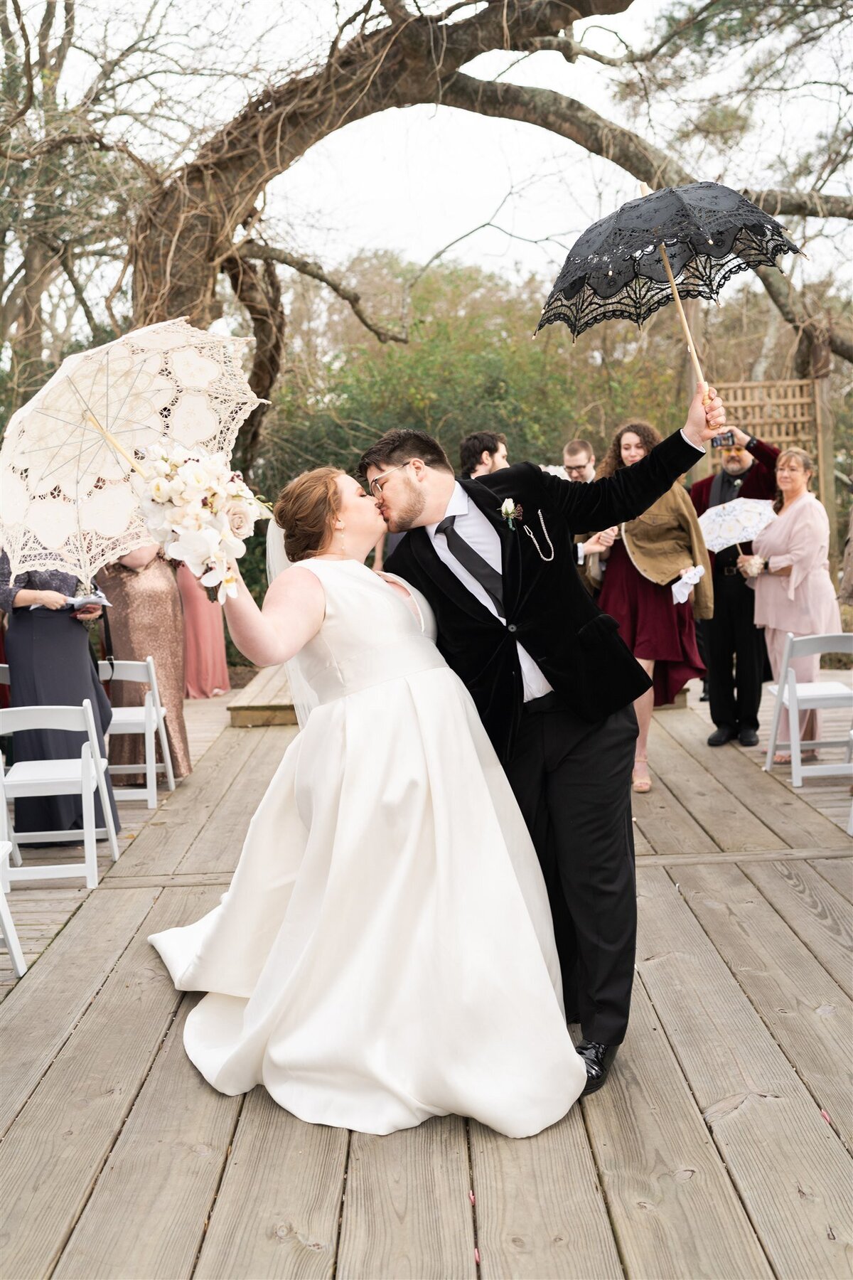 Bride and groom kiss at the end of the aisle with umbrellas.