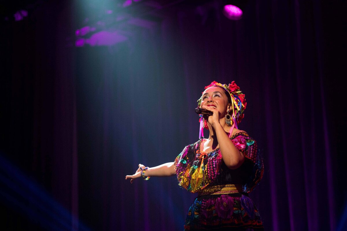 Mexican women in traditional clothes sings with dramatic stage light on her.