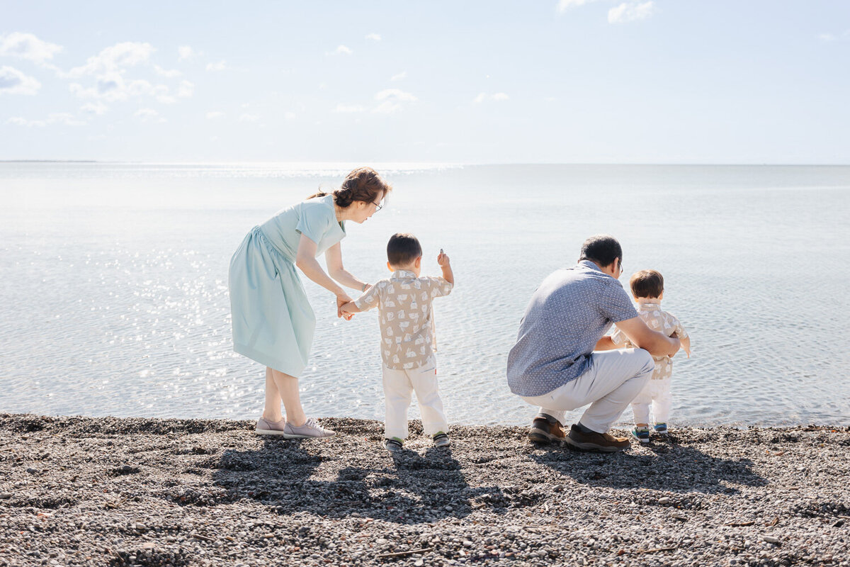 On a rocky Toronto Beach, a family of four, including two children and their doting grandparents, gather with sunlight dancing on the lake's surface—a perfect moment for Family Photography.