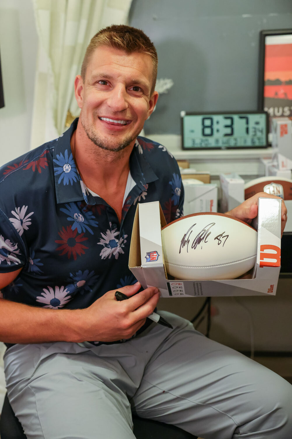 A man in a floral shirt is holding a signed rugby ball