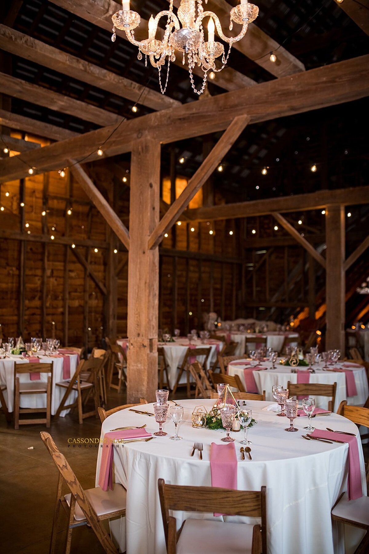 Wedding reception tables set with pink napkins inside a rustic barn.