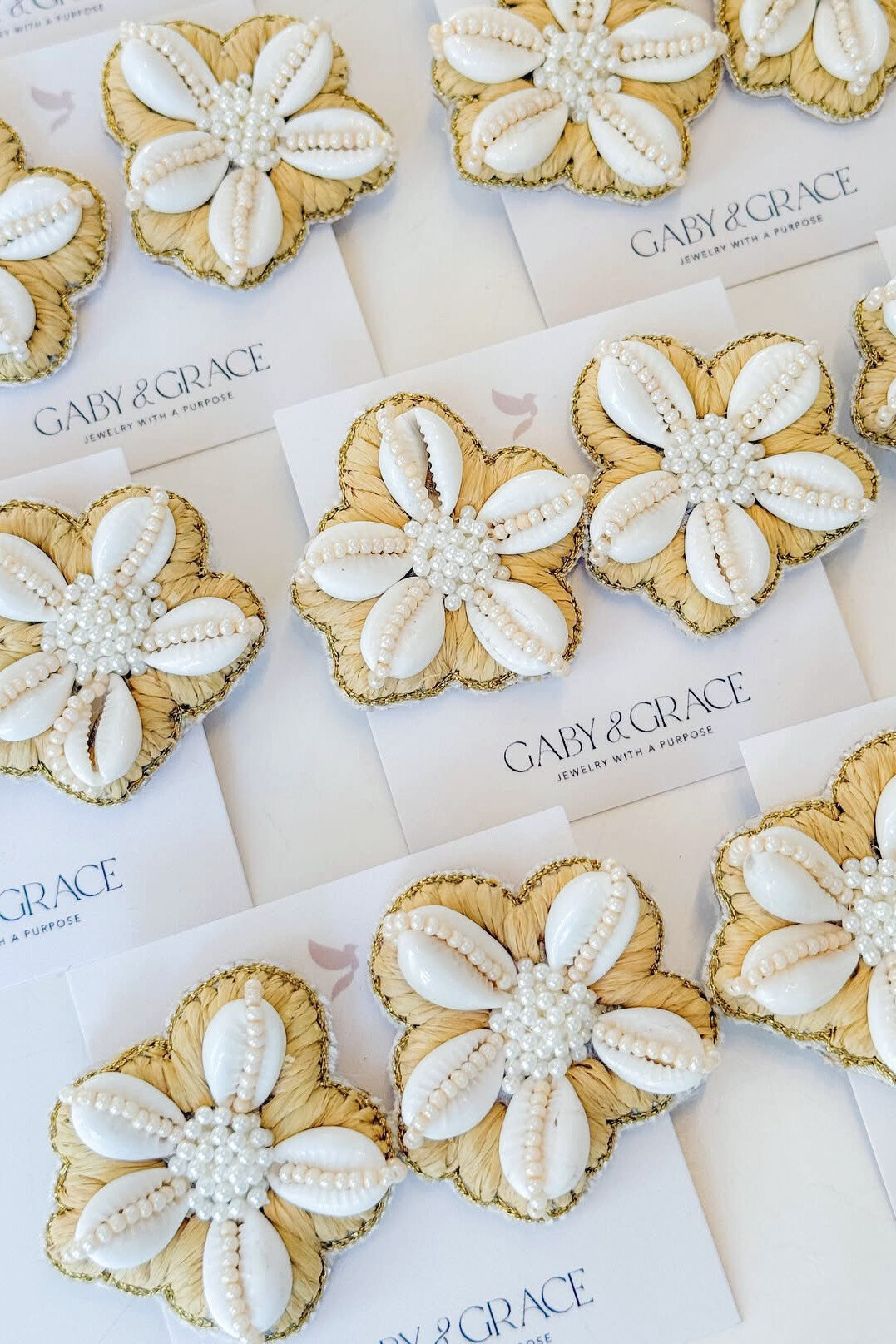 Collection of handcrafted earrings featuring cowrie shells and pearl beads, artfully arranged on Gaby & Grace branded cards.
