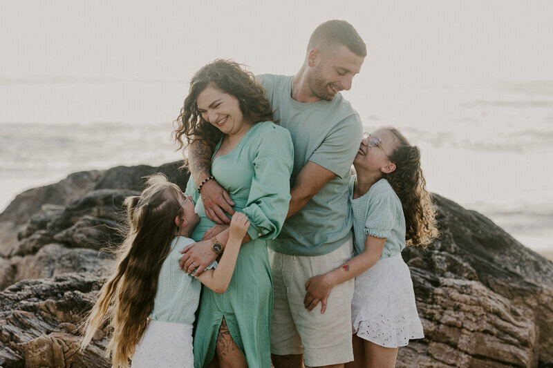 Famille habillée en vert et blanc se serrant dans les bras les uns des autres devant un décor de rocher te de mer lors d'une séance photo famille en Vendée.