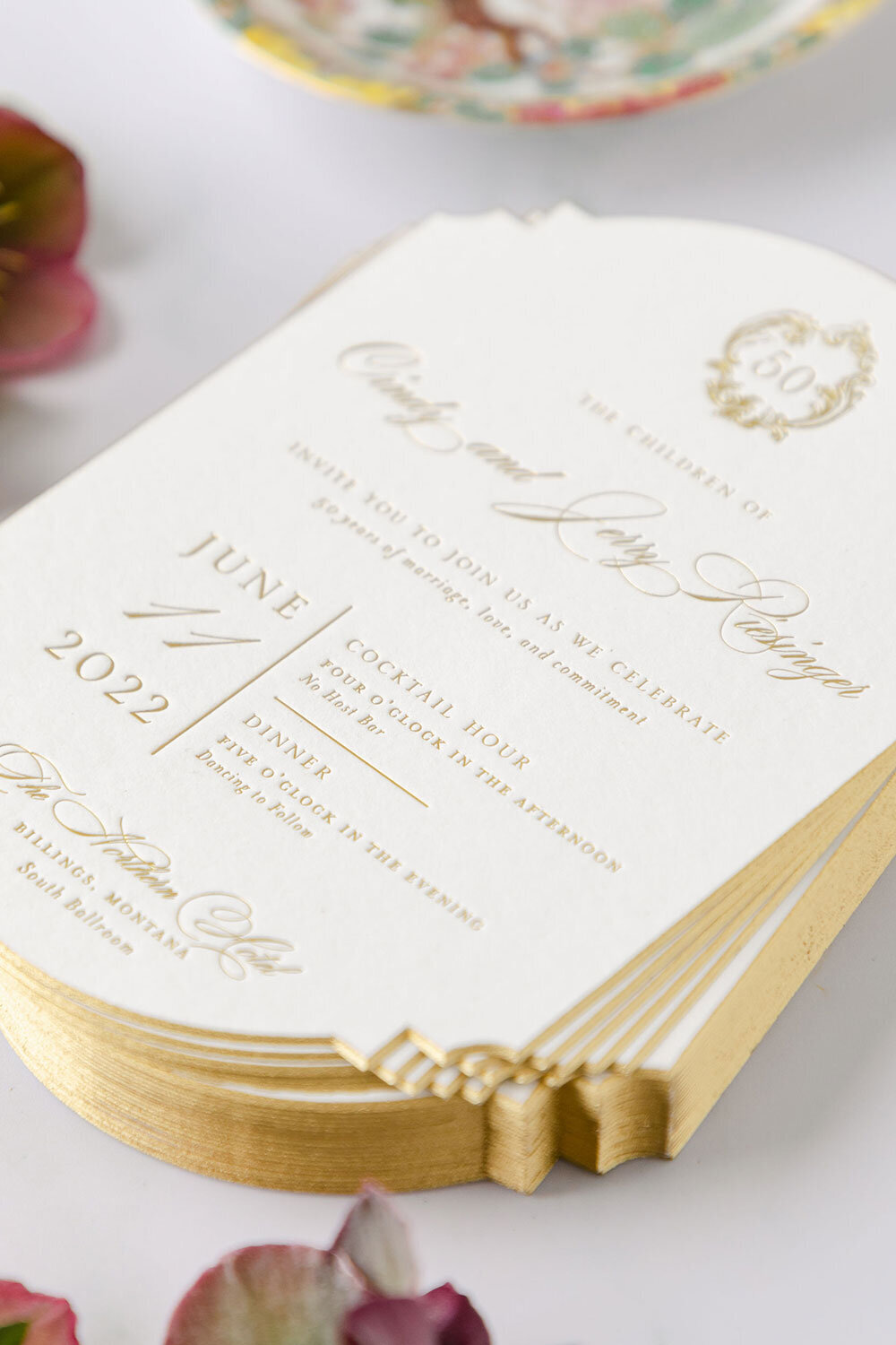 Gold foil wedding invitations with beveled edges and sculpted corners, featuring classic typography for a 50th anniversary celebration.