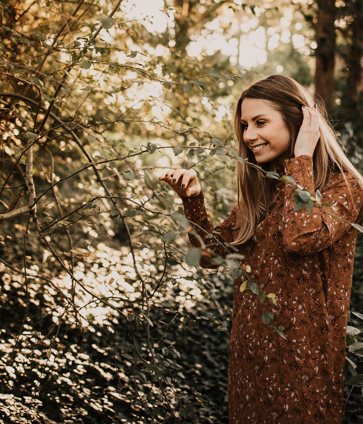 Barbora is surrounded by trees. She smiles and touches her hair