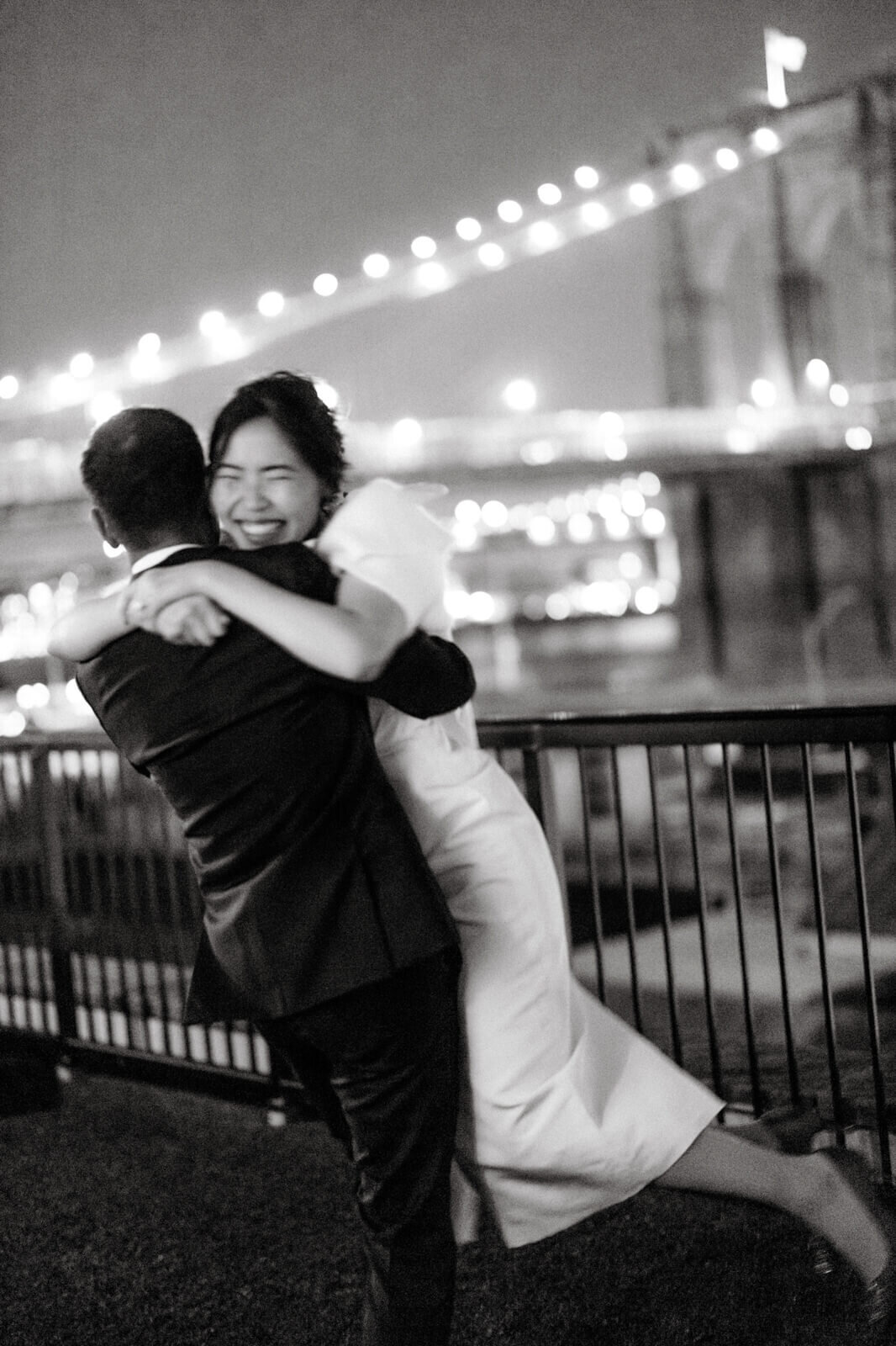 The groom hugging while carrying the bride in the air, on a veranda overlooking the Brooklyn Bridge.