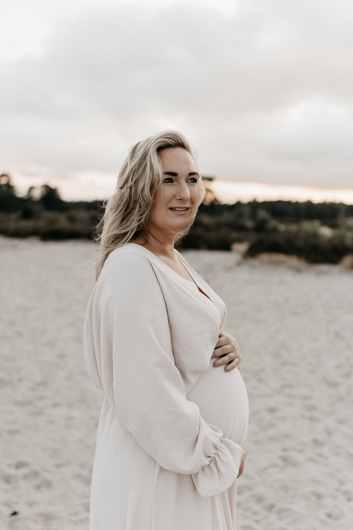 Zwangere vrouw houdt  buik vast tijdens zwangerschapsshoot in de Soesterduinen.