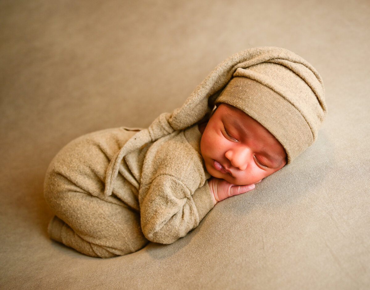 Photo by E. Benecki Photography during a  newborn photo session on the Kitsap Peninsula. Newborn posed sleeping on his belly with hands under his cheek. Baby dressed in tan outfit with matching sleepy cap.