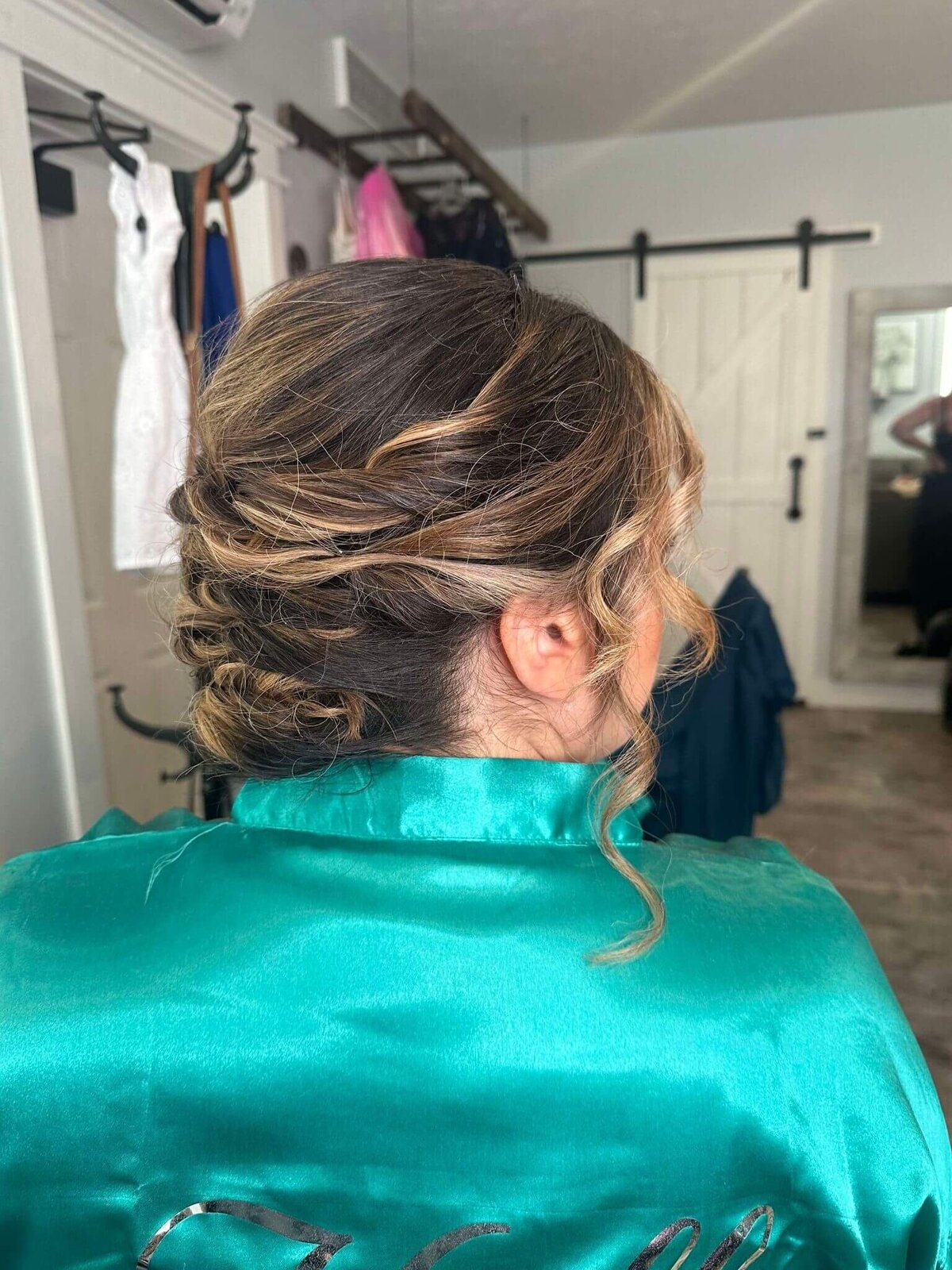 A woman with an elegant updo hairstyle, adorned with loose curls, wearing a satin robe, showcasing a beautiful look created for a special occasion by 212 Salon, Spa, & Barbershop.