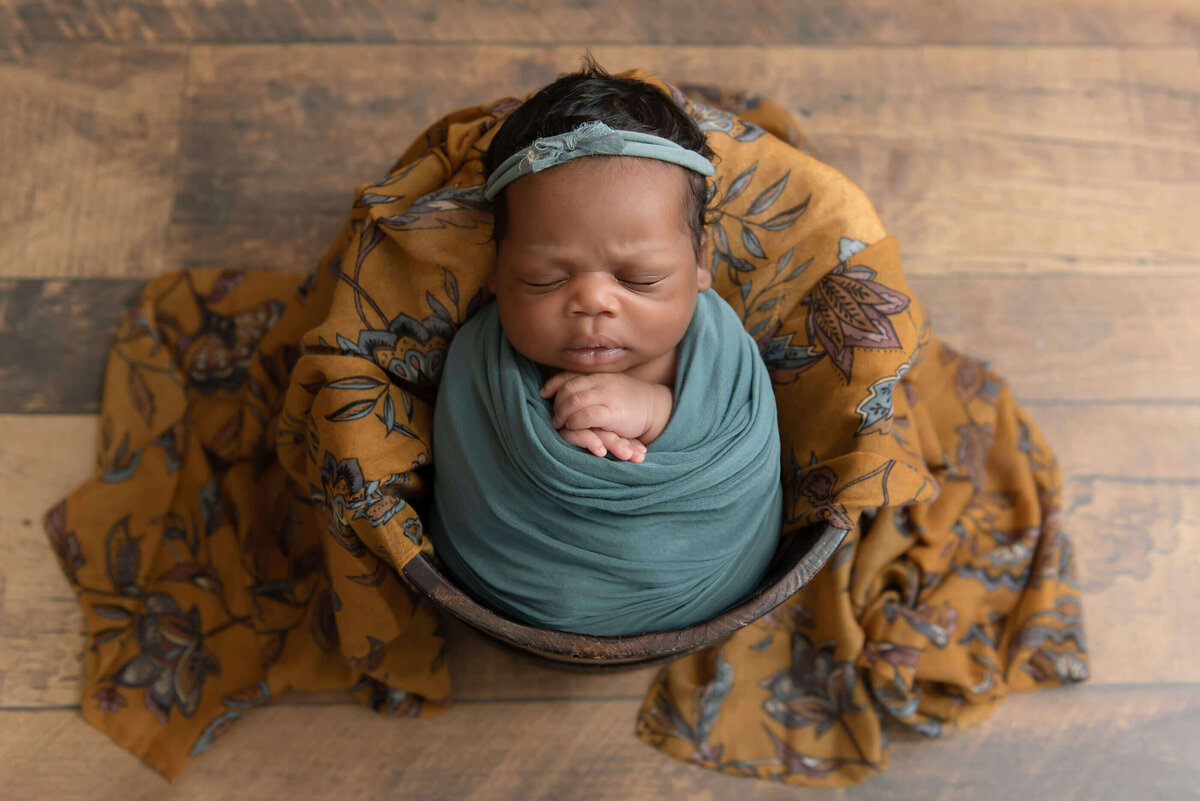 Black baby girl wrapped in green in a buck for her newborn photo session.