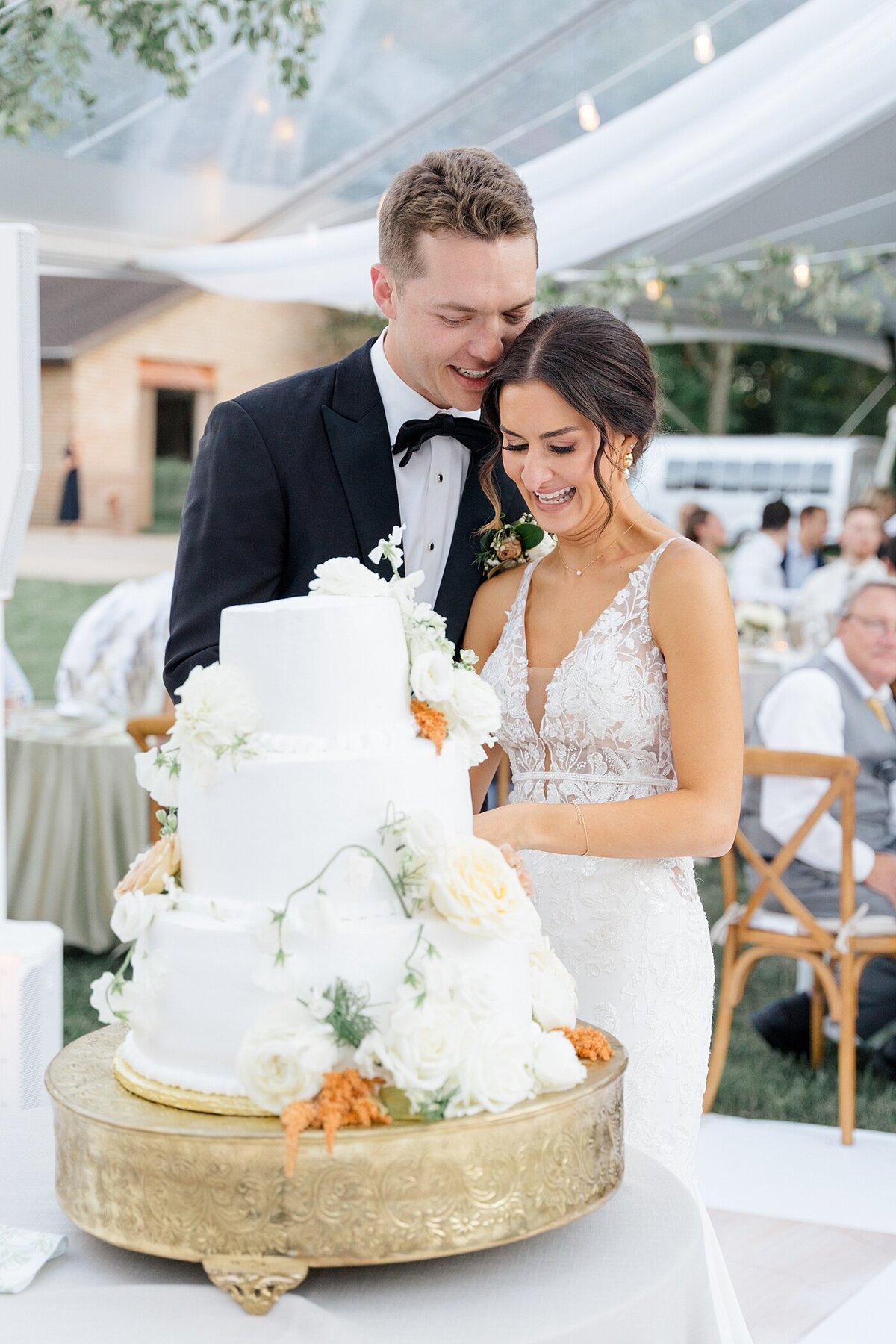 bride cutting the wedding cake while the groom leans into her and whispers in her ear during their wedding reception