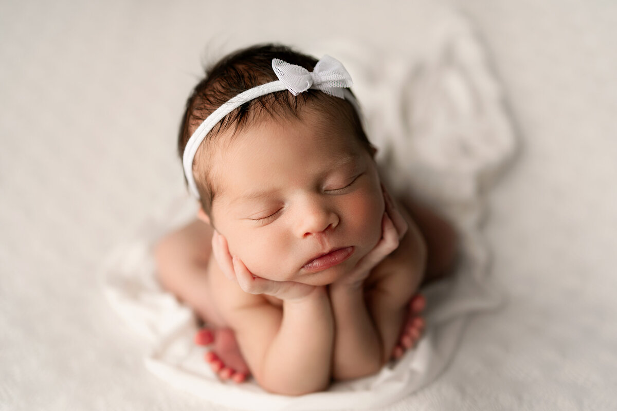 Newborn baby girl sitting with her head in her hands on a white blanket