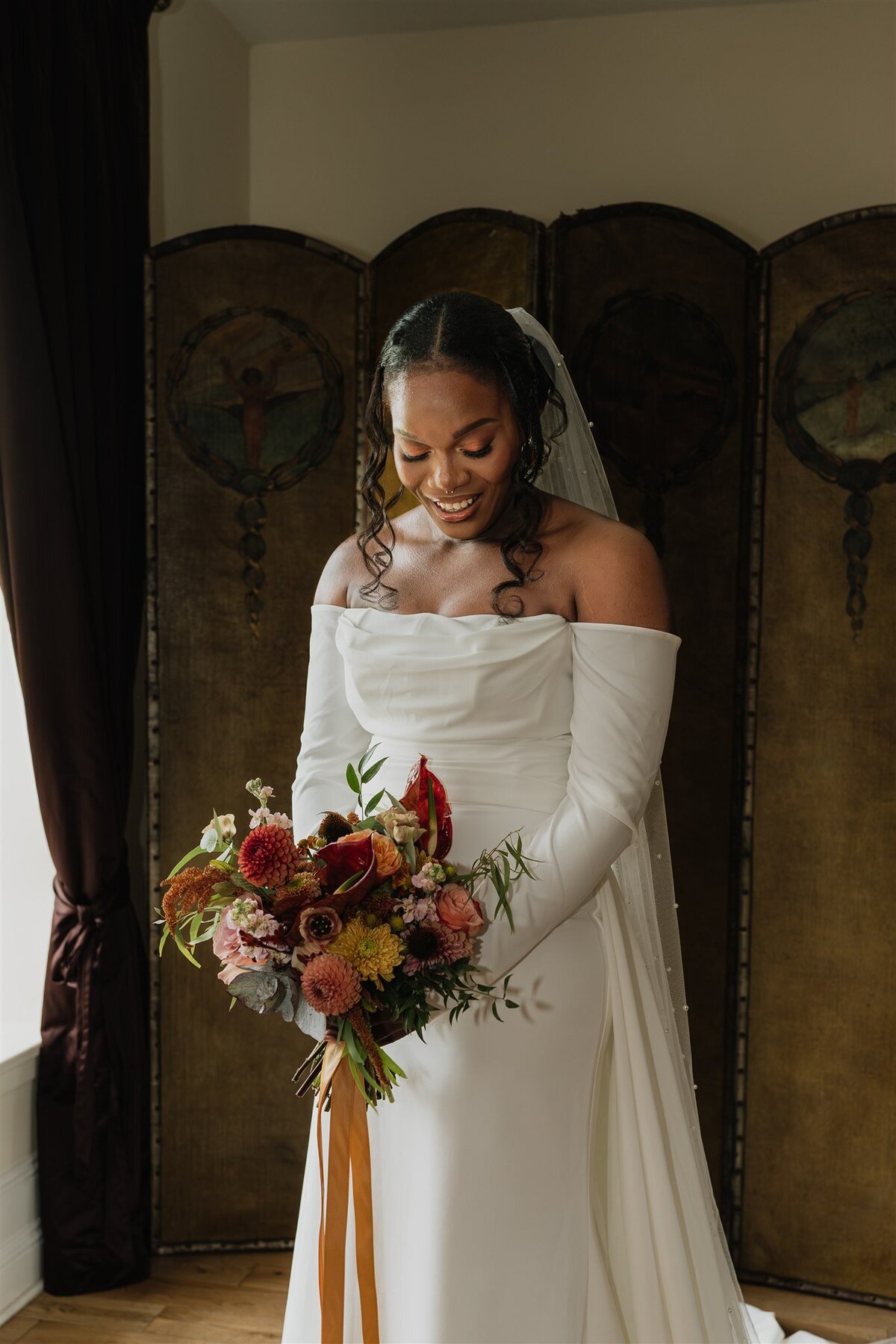 A bride wears a long white wedding dress and is photographed holding her bouquet in the bridal suite of Logie Country House.