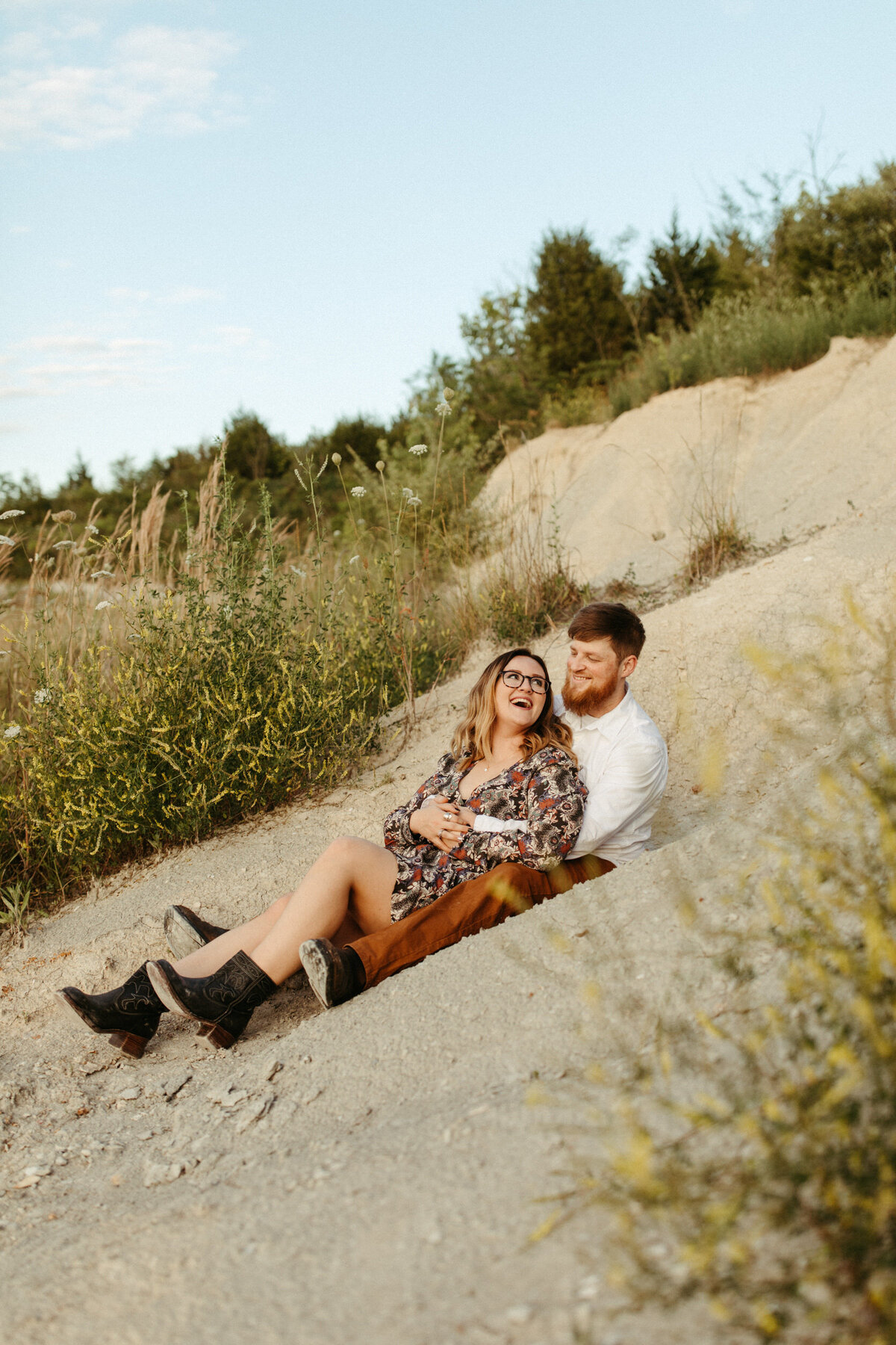 Couple sitting on sand dunes looking at each other and laughing
