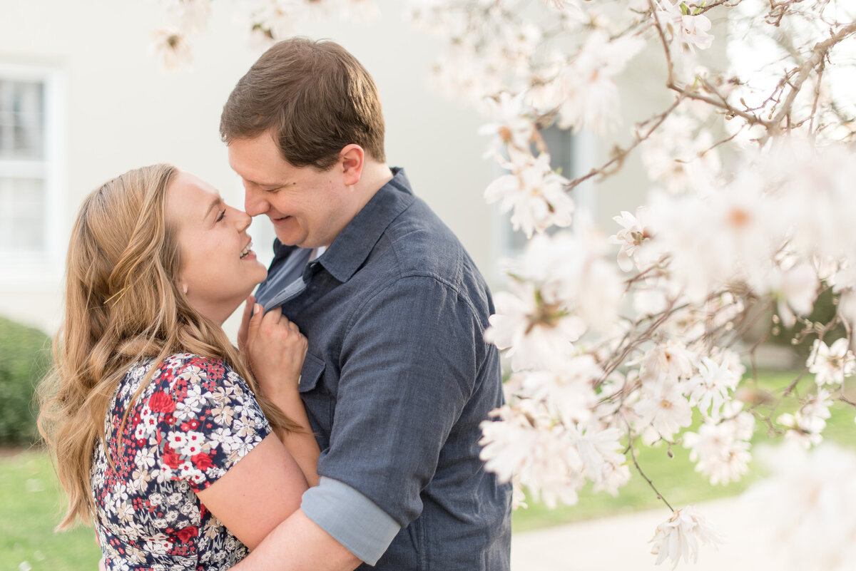 Engaged couple hugging tightly and almost kissing as they smile beside tree blooming white flowers in Lancaster, Pennsylvania.
