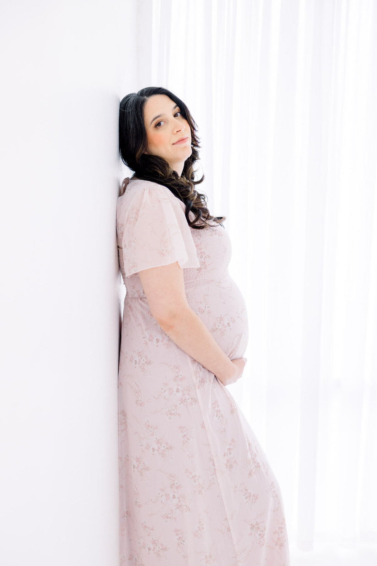 Pregnant woman with dark hair leaning against wall for Tampa maternity photographer Tina Marie Studio.