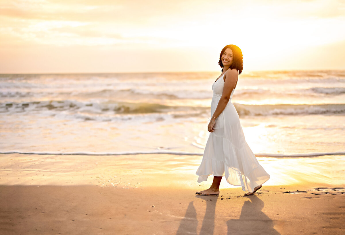 Golden hour senior photo of a girl walking on the beach at sunrise, glowing with confidence and artistic movement.