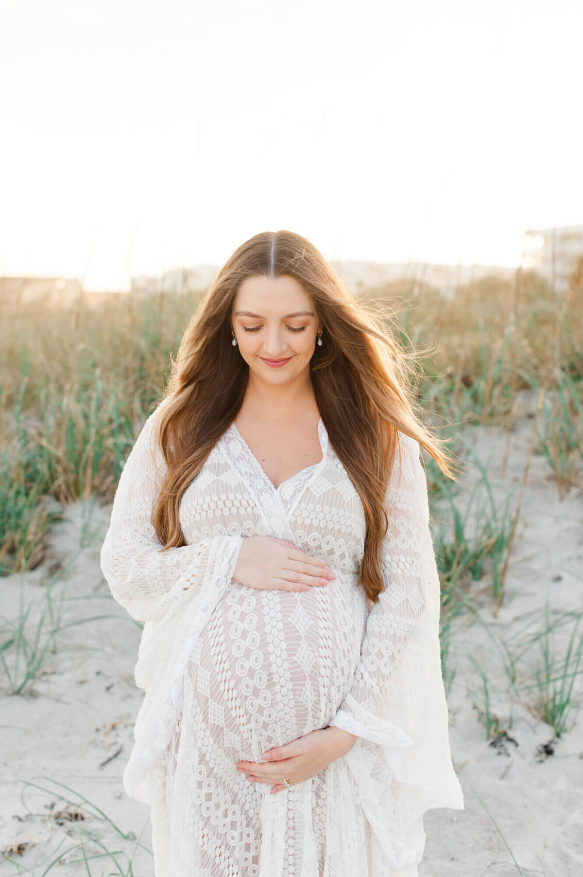 Single portrait image of a beautiful pregnant mom holding her belly and looking down toward her belly in golden hour light