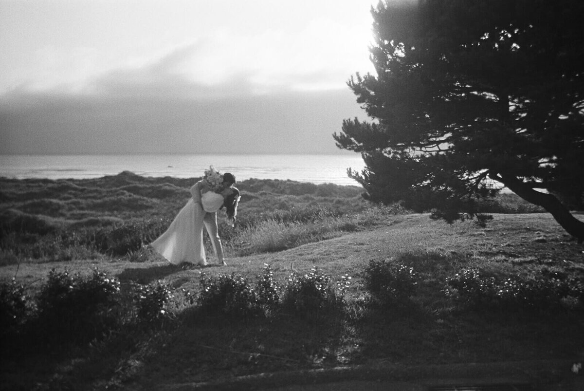A groom bending his bride and kissing her at the Oregon Coast, in black and white. 