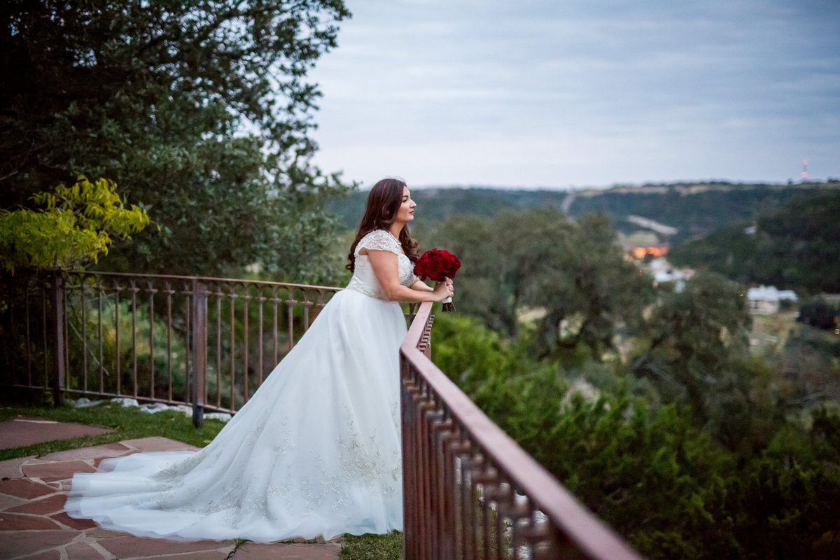 Bride looking over cliff edge and leaning on railing while posing for her bridal photography session.
