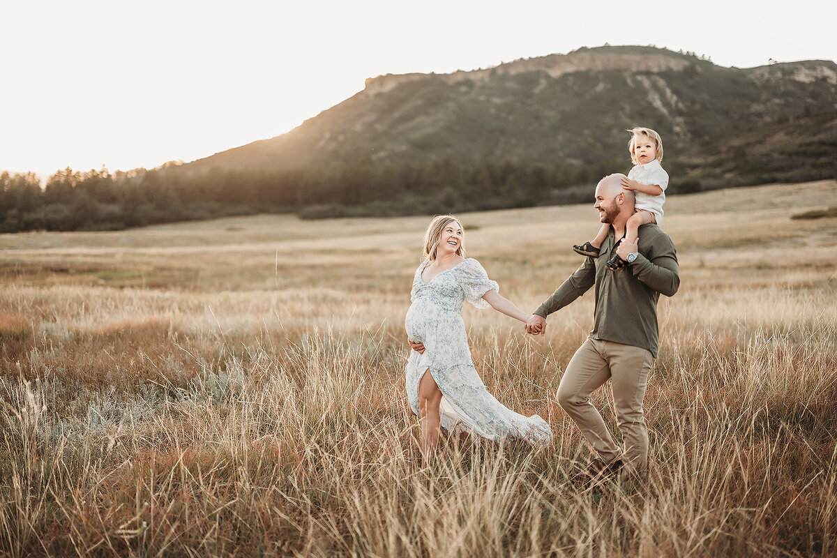 pregnant woman leading her husband and son through the field while looking at toward them