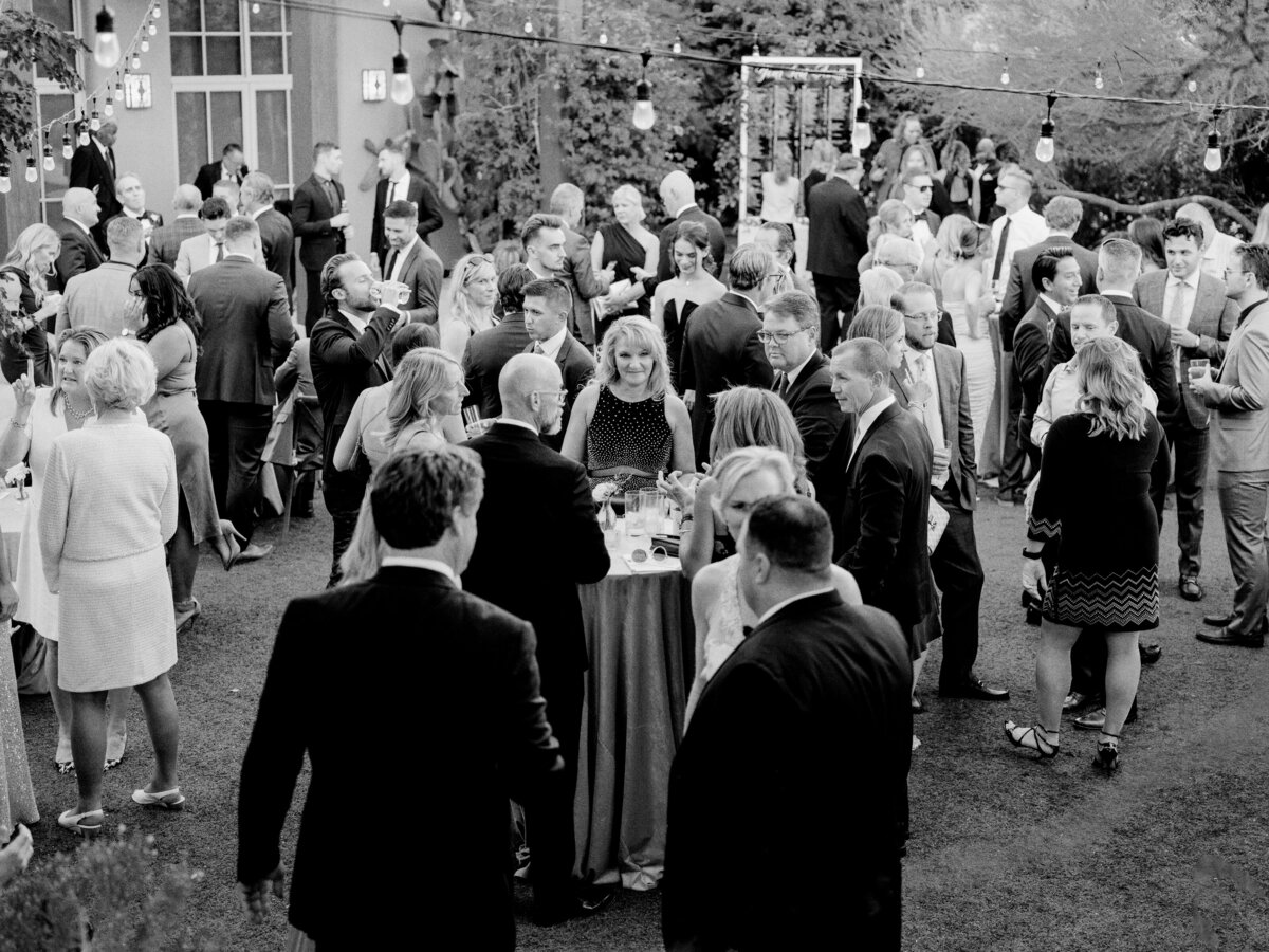 Wedding guests enjoy a lively cocktail hour at an elegant outdoor reception, surrounded by twinkling lights and beautiful scenery. A joyous start to the celebration.