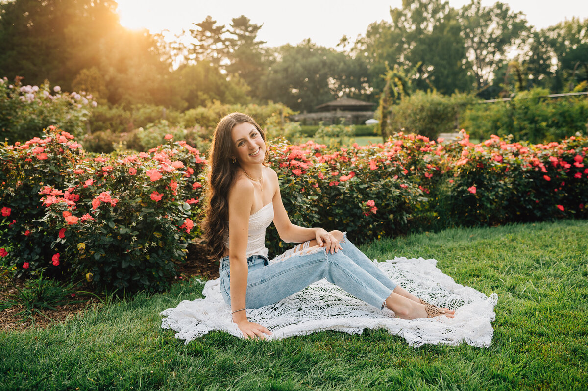 A high school senior girl sitting in a garden with a white tank top