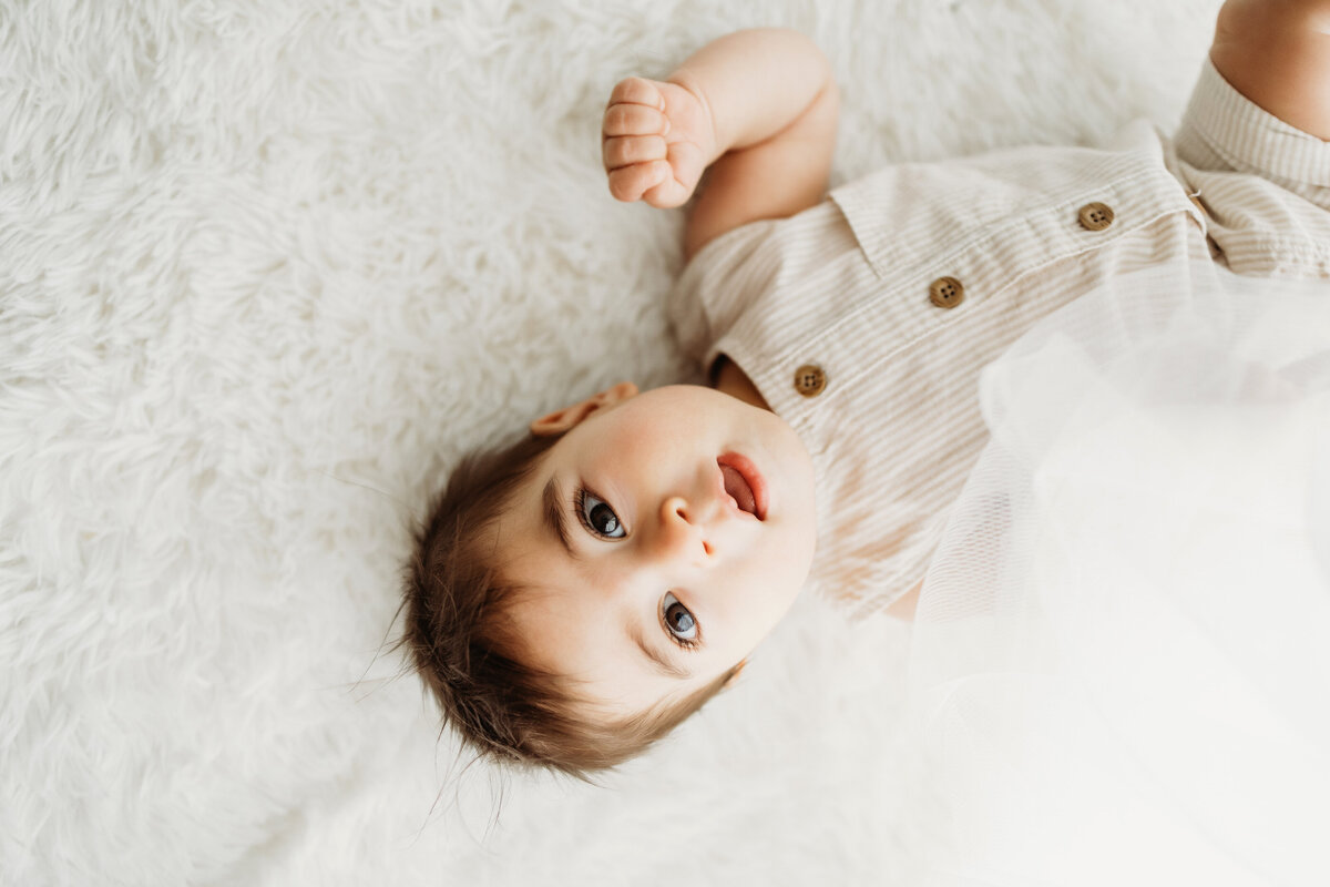 Six month old baby boy laying on his back in a white romper for his sitter milestone session in Denver