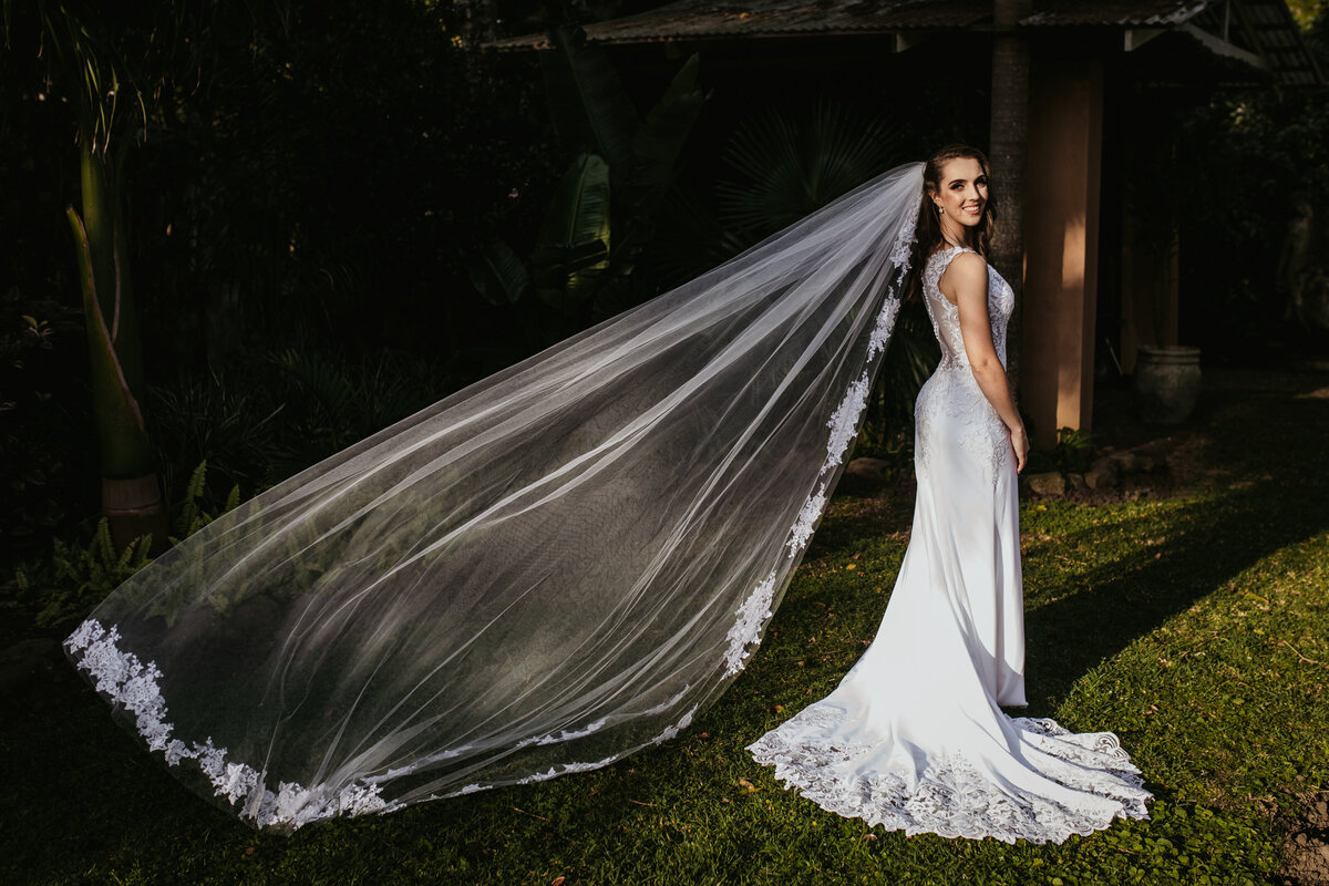 The bride stands in the garden with a veil blowing in the wind. 