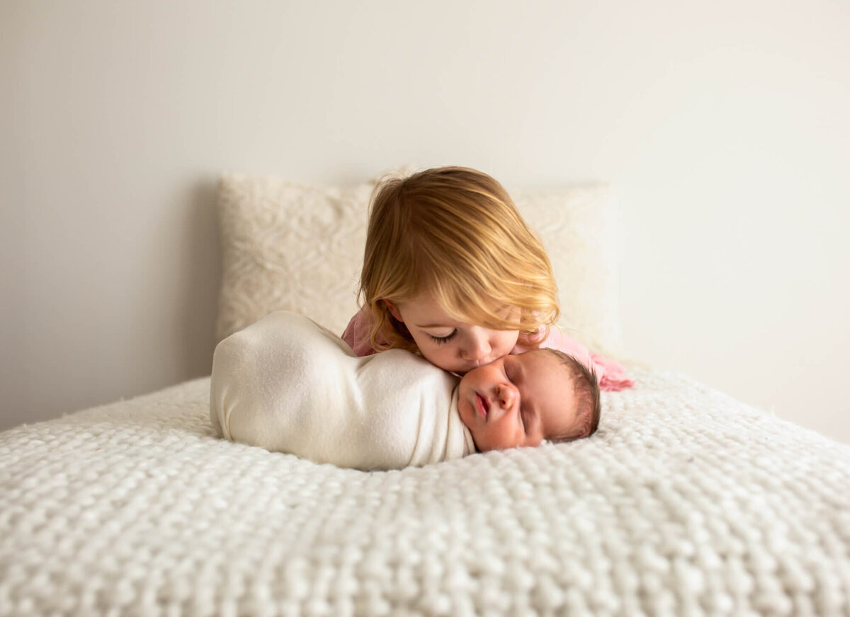A new big sis gives a kiss to her newborn baby brother while laying on a blanket at an asheville portrait studio