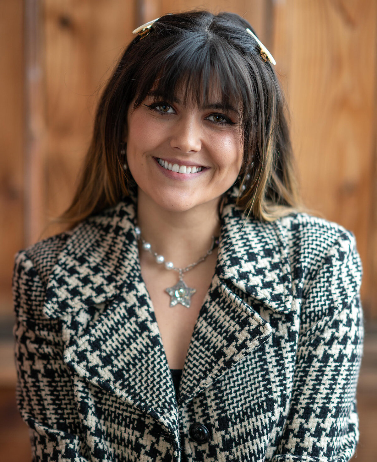 Close-up image of a young woman smiling with long, dark hair in a plaid jacket