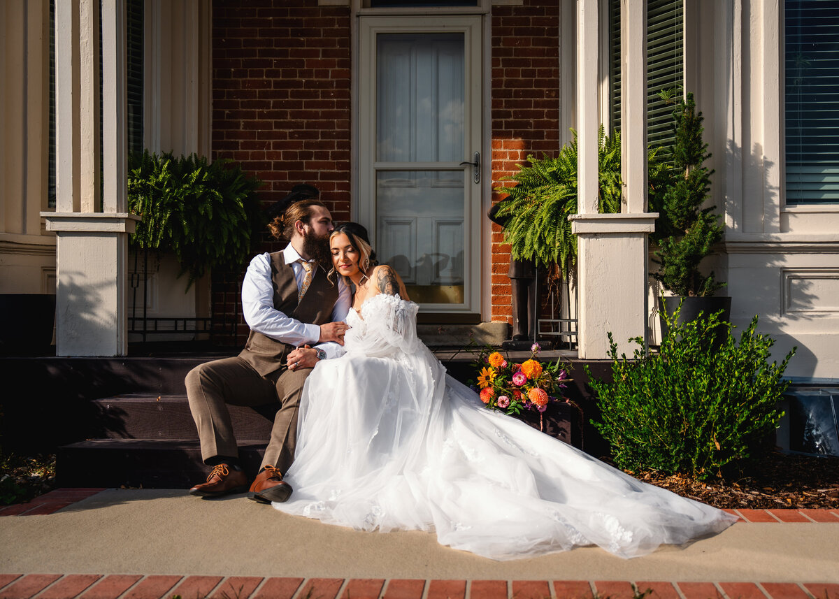 fine art wedding photography of a couple on their wedding day seated on the stairs of their wedding venue at 1886 Farmhouse in Boone Iowa near Des Moines Iowa