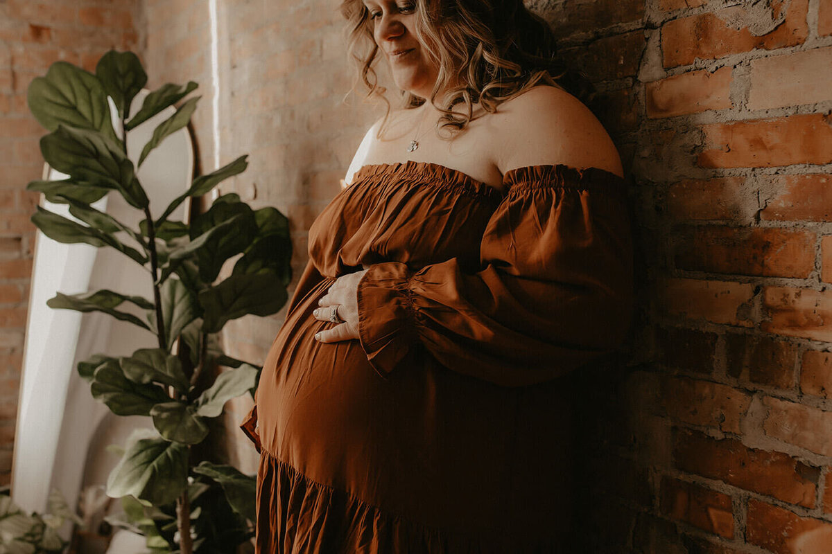 A close up of a pregnant mom leaning against a brick wall in a studio in canandaigua ny